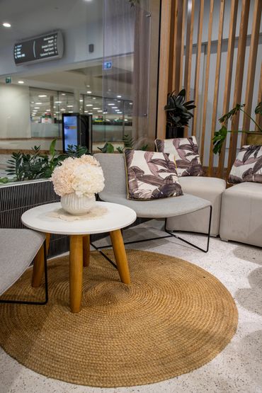 Retail waiting area with grey chairs, coffee table and rattan rug.