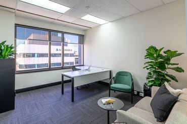 Office space with L shaped desk, tambour unit, green armchair and grey lounge with black side table.