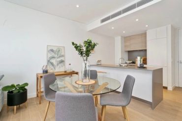 Open plan kitchen and dining area featuring glass dining table and grey upholstered chairs.
