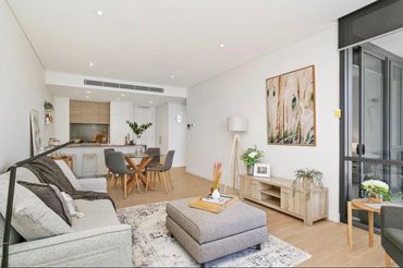 Open plan kitchen, dining and living area with grey sofa, artwork and greenery throughout.