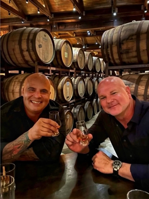 Two men enjoying whiskey tasting in a barrel room.