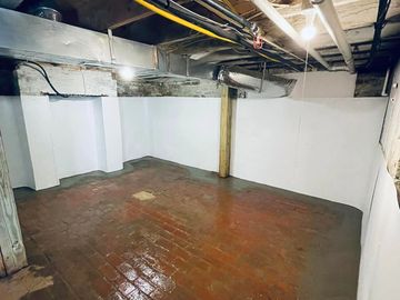 Empty basement with brick floor and exposed pipes overhead.