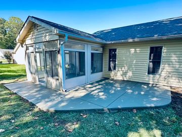 Concrete patio adjacent to a screened porch on a house's backyard.