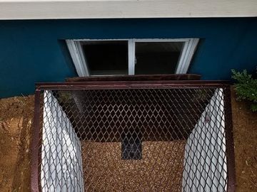A basement window well with a protective metal grate.