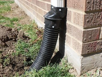 Black flexible downspout extension attached to a white gutter on a brick house corner.