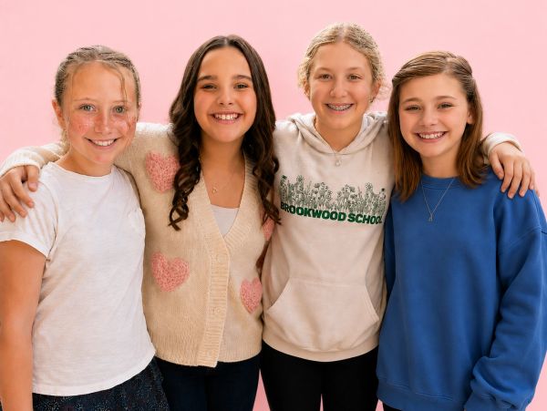 Four smiling girls standing arm in arm against a pink background.