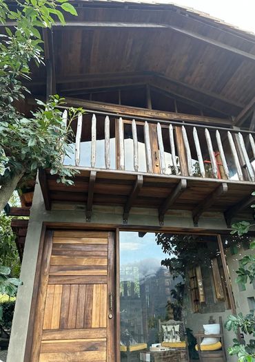 Rustic two-story house with wooden balcony and large glass door.