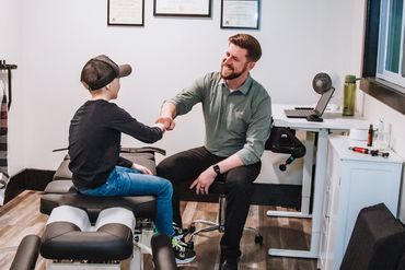 Chiropractor shaking hands with a young patient in a clinic room.