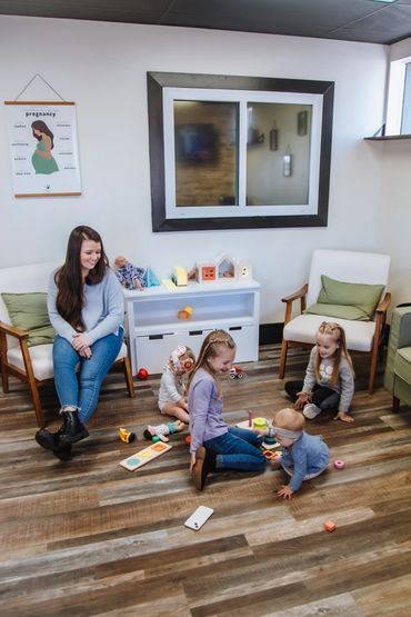 Woman watches children playing with toys in a cozy room.