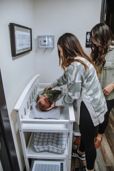 Two women attending to a baby on a changing table in a restroom.