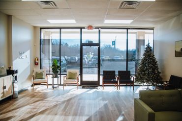 Bright waiting room with chairs, a Christmas tree, and large glass windows.