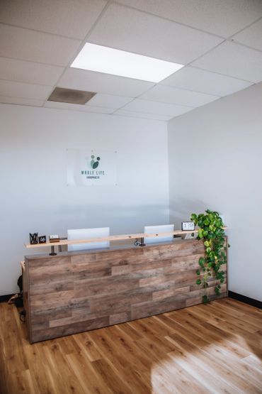 Reception desk in a clean chiropractic office with a plant and calendar.