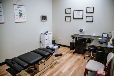 A clean chiropractic office with a treatment table and certificates on the wall.