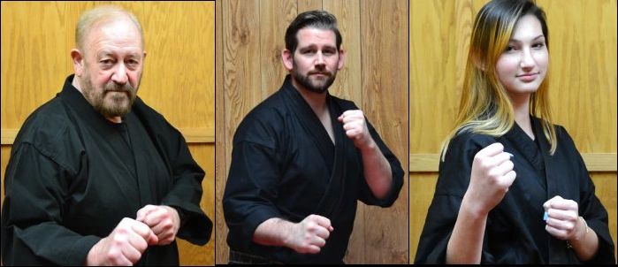Three people in black martial arts uniforms posing with fists up.