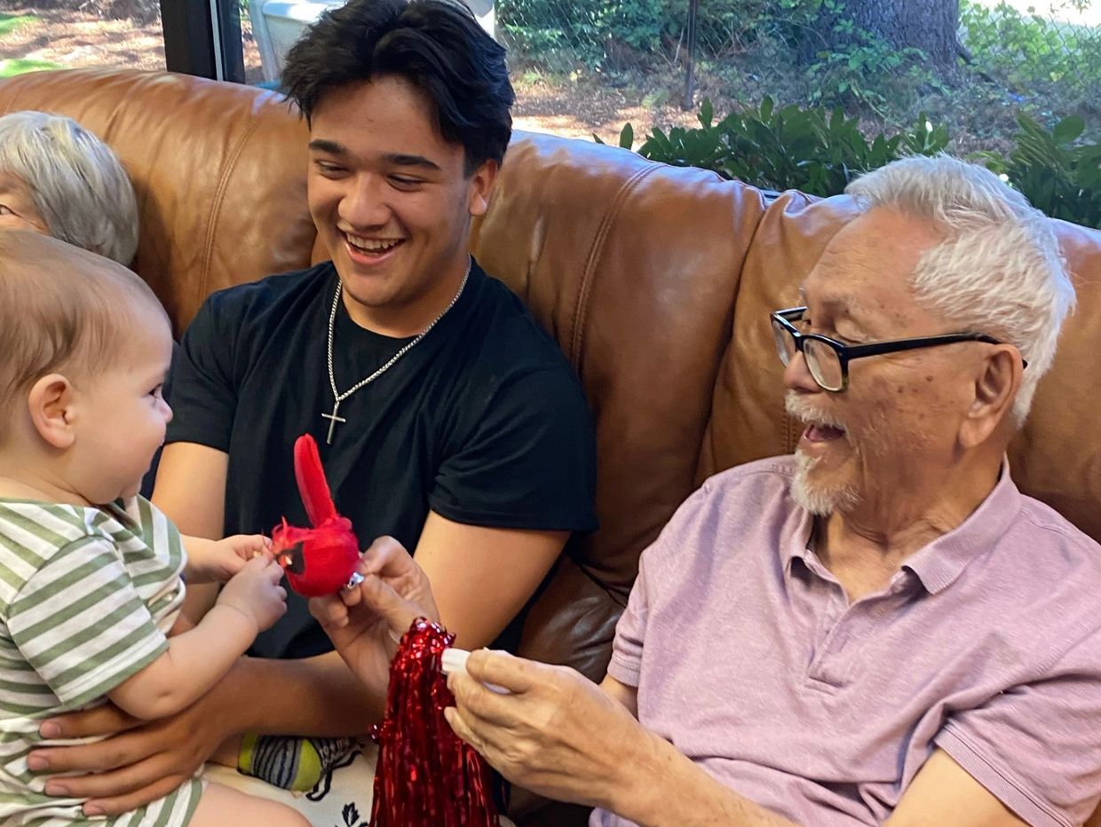 A senior and caregiver smile as they play with baby at an Intergenerational daycare in Tigard, OR.