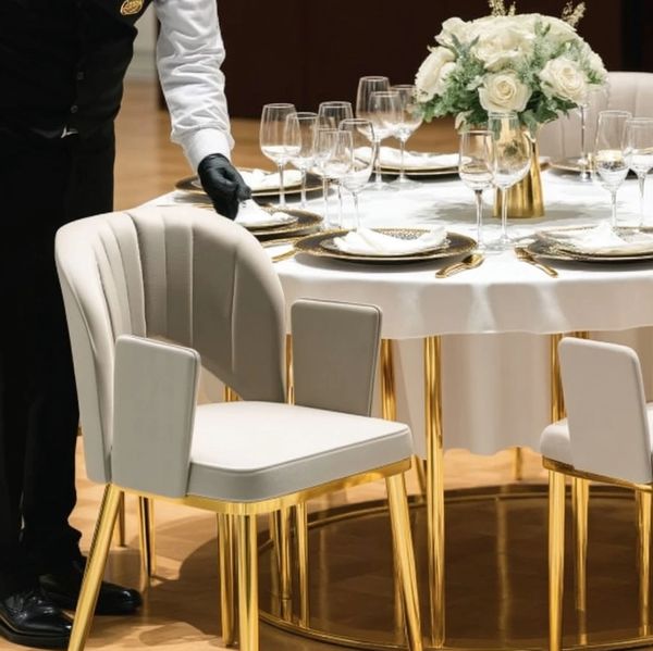 Elegant dining setup with gold-accented chairs and table, and a waiter arranging napkins.