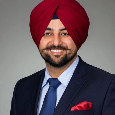 Smiling man wearing red turban and navy blue suit.