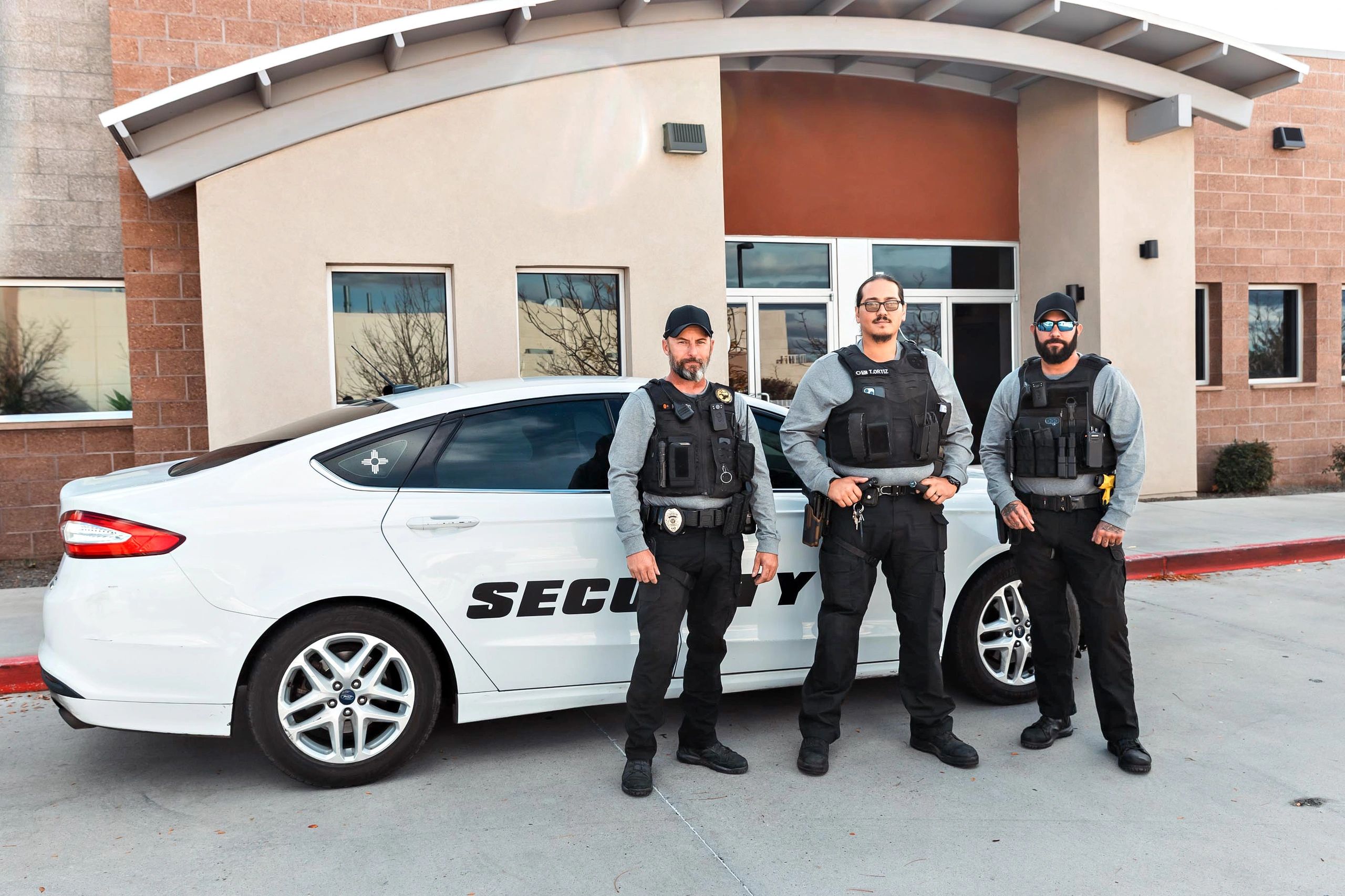 Three security guards standing in front of a security vehicle outside a building.