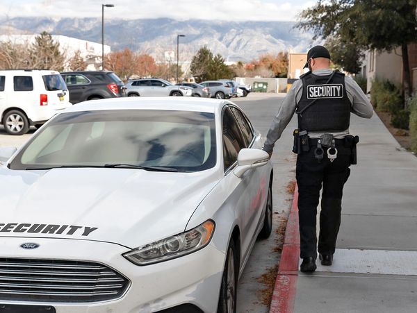 Security guard walking beside a white security car in a parking area. Guard cleared the area of threats