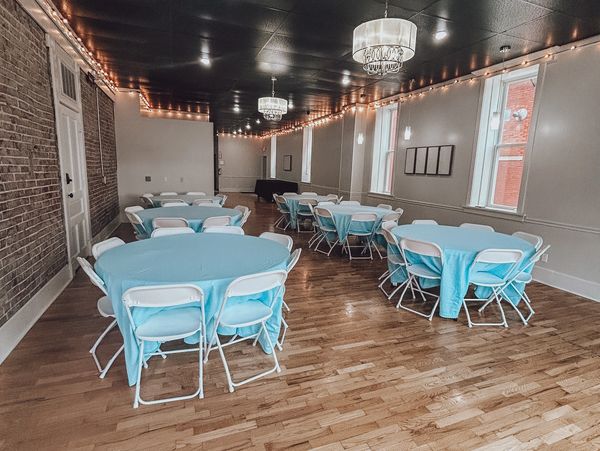 Event room with round tables and blue tablecloths under elegant chandeliers.