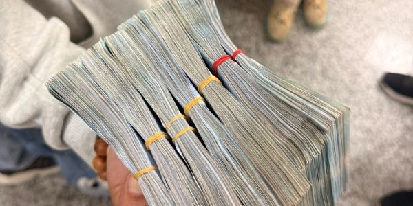 Hand holding several thick stacks of bundled money.