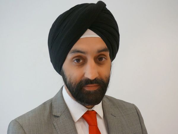 Man wearing a black turban and gray suit with a red tie.