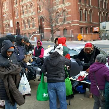 People gathered outdoors, receiving clothes and supplies near a city street.