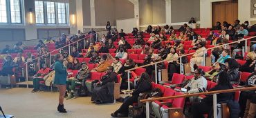CEO & Clinical Director, woman Dr. Dicks speaks to a large audience in a lecture hall.