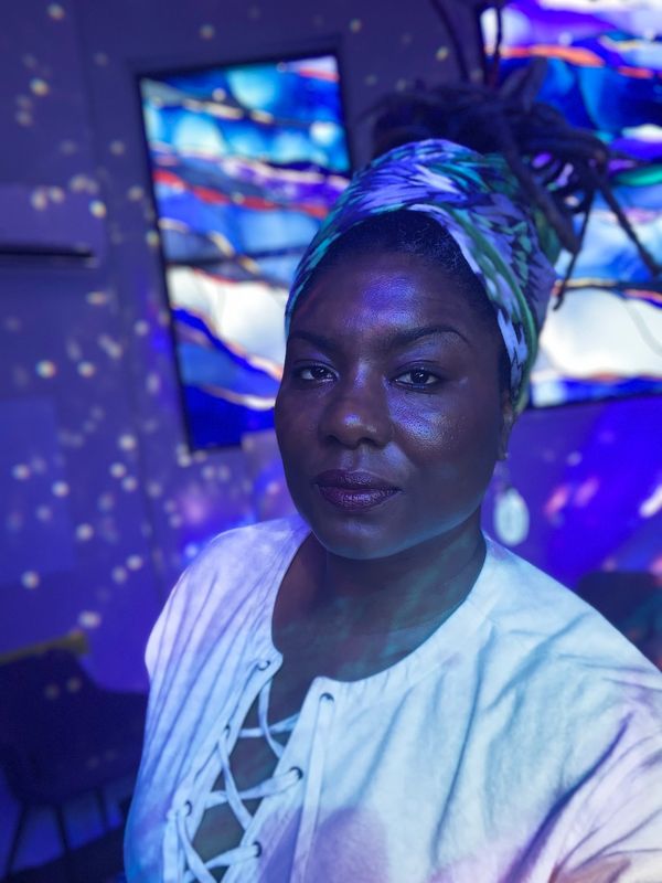 Woman Maisha-Atrice with a colorful headwrap in blue lighting.