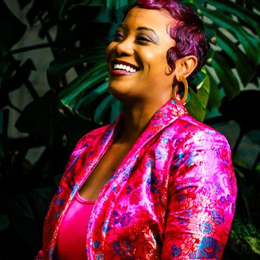 Woman Dr. Dicks smiling in a vibrant pink floral blazer.