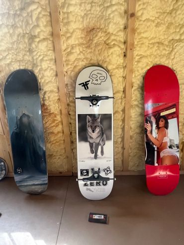 Three skateboard decks with unique designs leaning against a wall with yellow insulation.