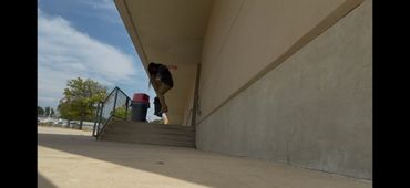 Skateboarder performing a trick down a set of stairs near a building.