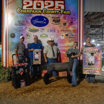 Group at 2025 Champaign County Fair with sheep and award banners.