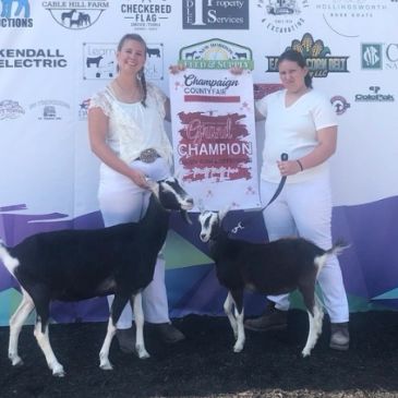 Two women posing with goats and a champion banner.