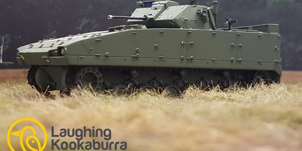 Model of a military tank on grass with a forest background.