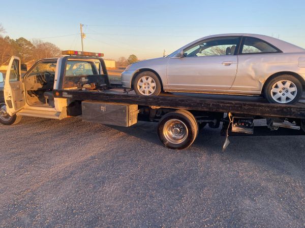 A damaged silver car on a tow truck at sunset.
