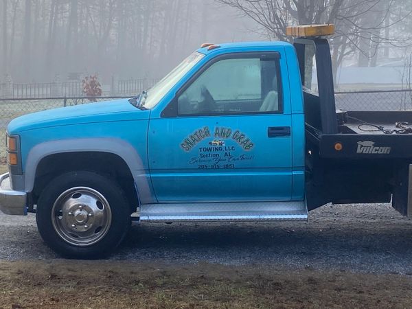 Blue tow truck parked on a foggy day beside a fence.