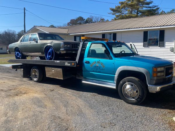A blue tow truck carrying a vintage car with blue wheels.