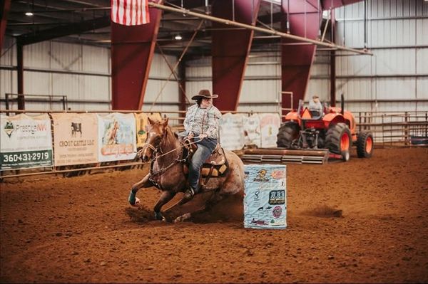 Cowboy riding horse around barrel in arena.