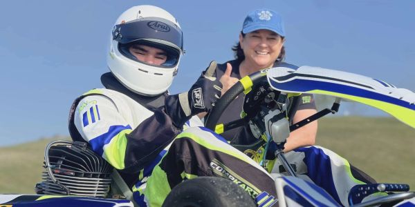 Go-kart racer giving a thumbs-up with a smiling woman beside him.
