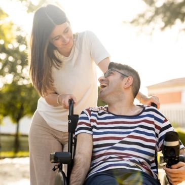 Woman pushing man in wheelchair outdoors, both smiling.
