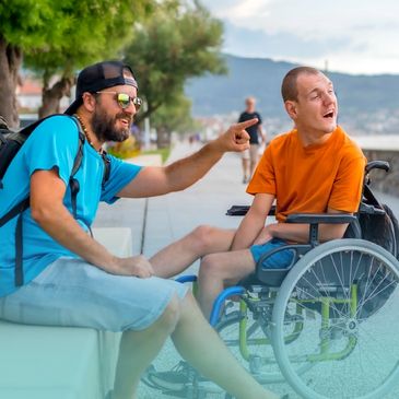 Man in blue shirt and man in orange wheelchair share a moment outdoors.