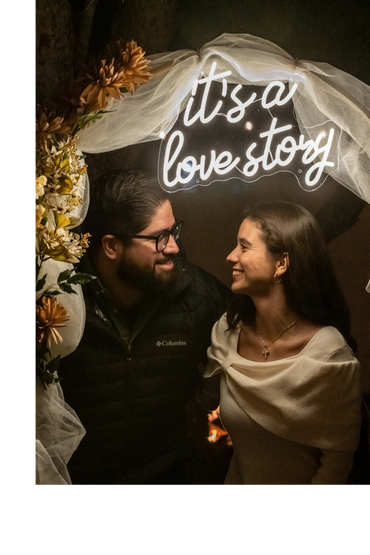 Pareja posando en un set romántico iluminado con letrero decorativo durante una velada especial al a