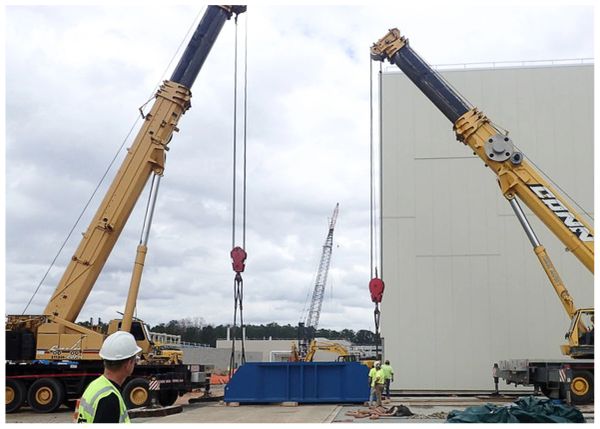 Two cranes lifting a large blue container at a construction site.