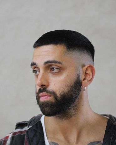 Man with a fade haircut, beard, and plaid shirt looking sideways.
