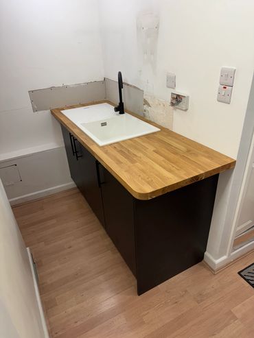 Newly installed kitchen sink and wooden countertop in a small space.