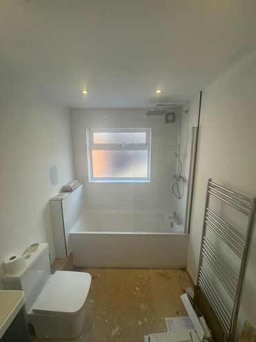 Minimalist bathroom with bathtub, toilet, and heated towel rail under warm lighting.