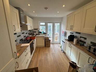 Modern kitchen with cream cabinets and wooden countertops, featuring a glass door leading outside.