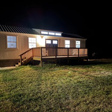 A well-lit house with a wooden porch at night in a grassy area.