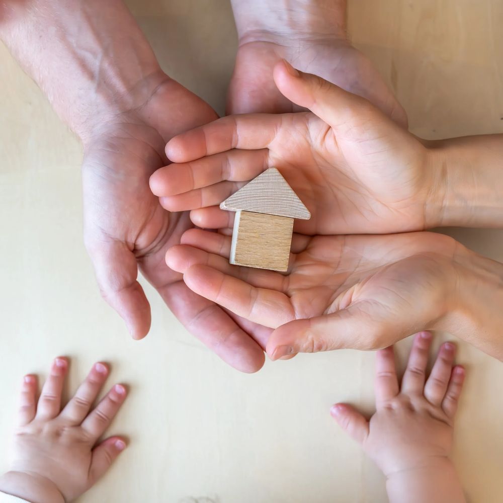 Adult and child hands holding a small wooden house model together.